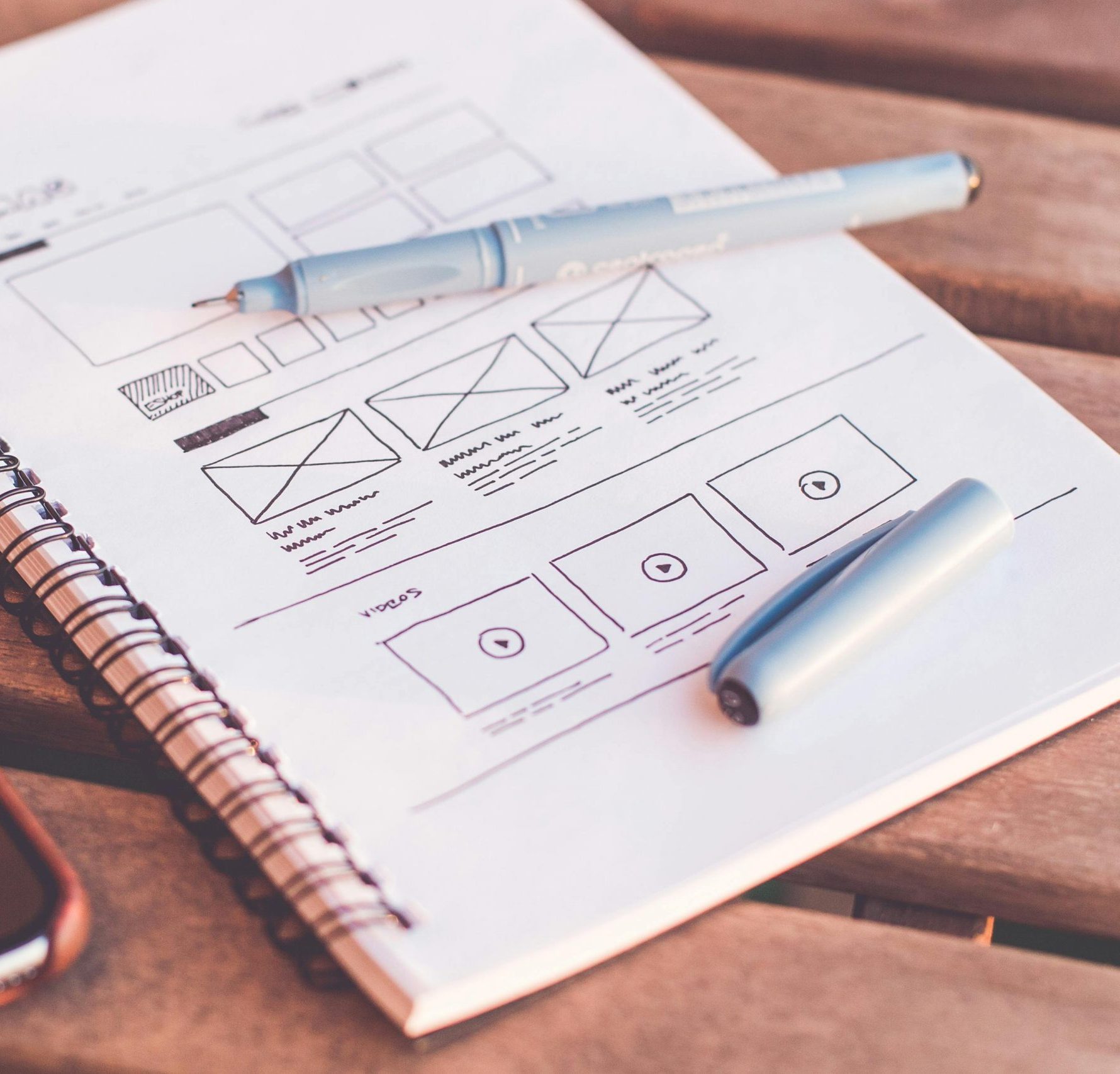 Close-up of a notebook with wireframe sketches and a smartphone on a wooden desk.
